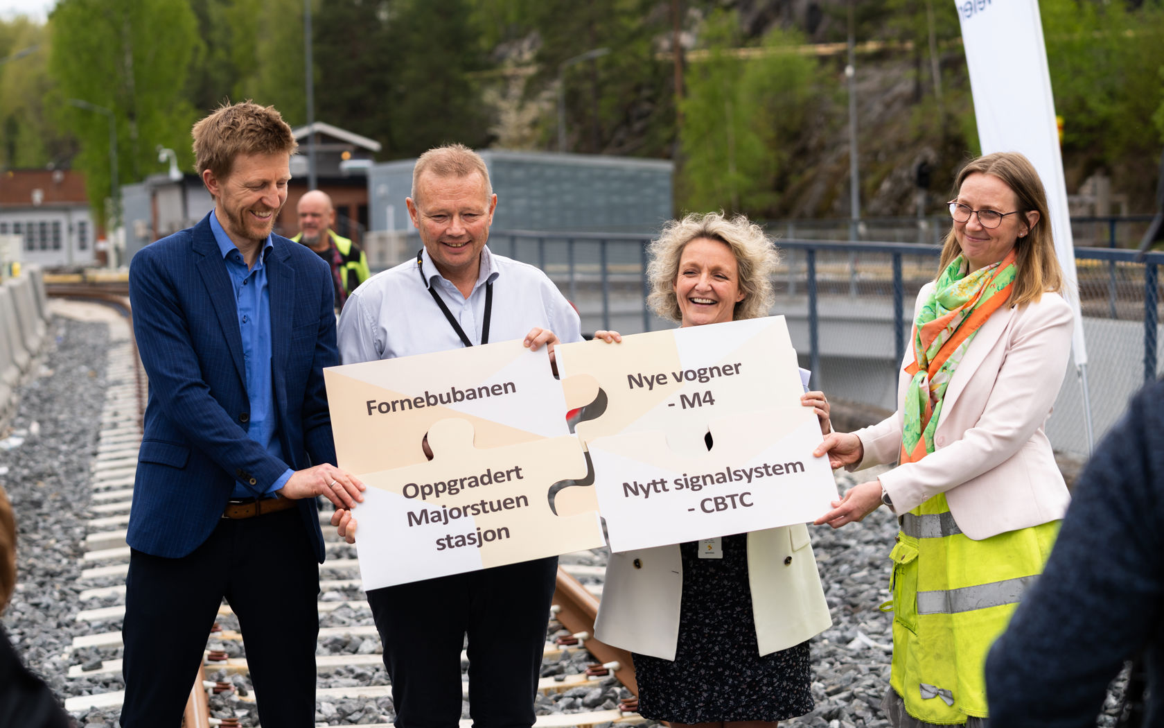 Bildet viser fire mennesker som holder frem et puslespill i papp, der hver brikke har navnet til en av de fire prosjektene som utgjør T-baneløftet.