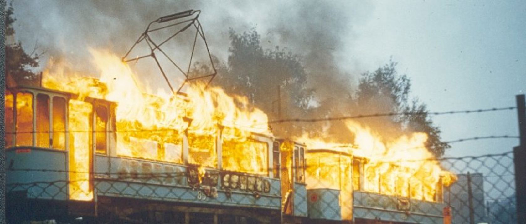 En eldre trikk i med masse flammer som skyter ut gjennom alle vinduene.