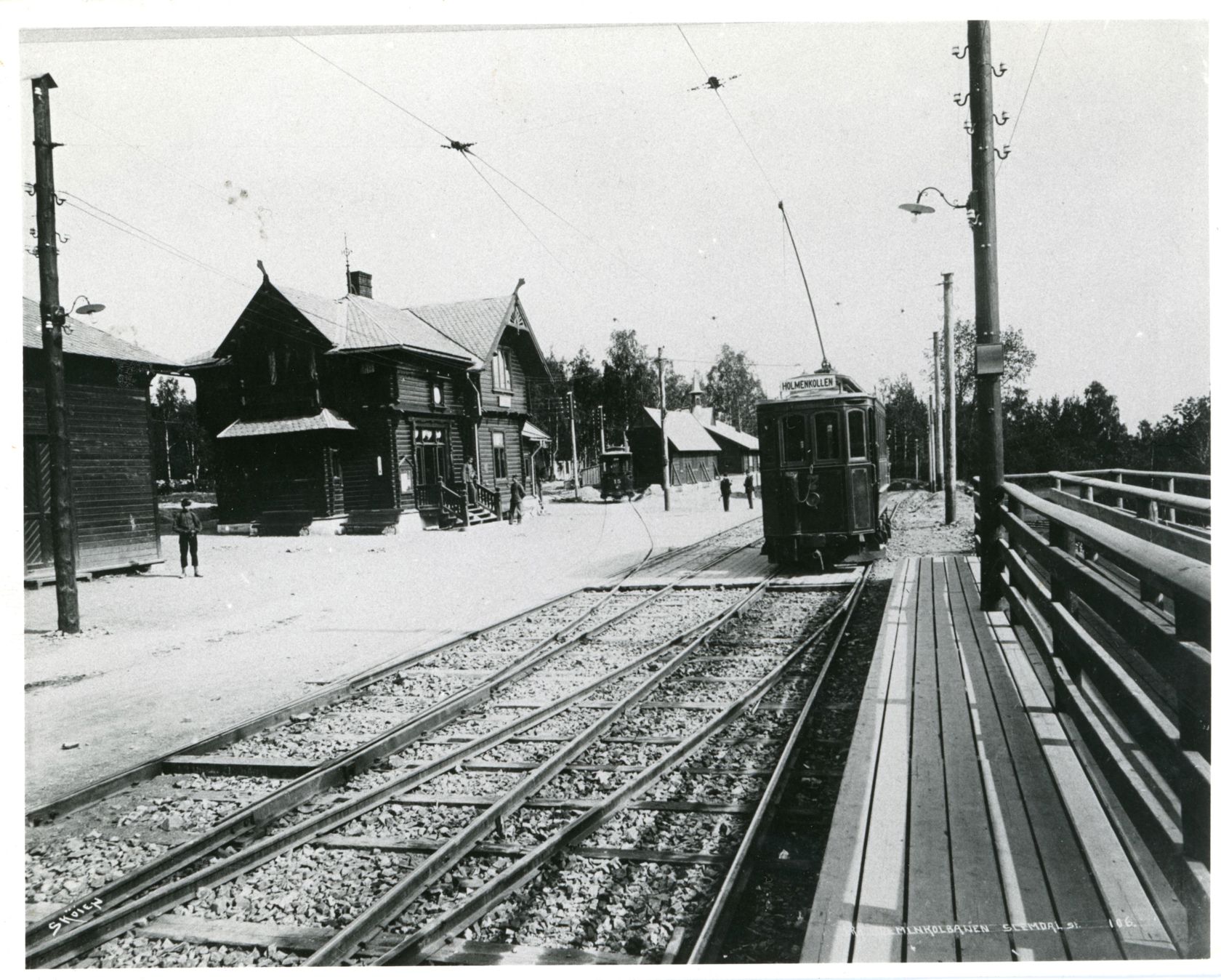 Sort-hvitt bilde av trikken til høyre. Et eldre trehus til venstre.